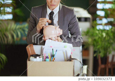 Modern woman worker in green office putting coin into piggy bank 109832373