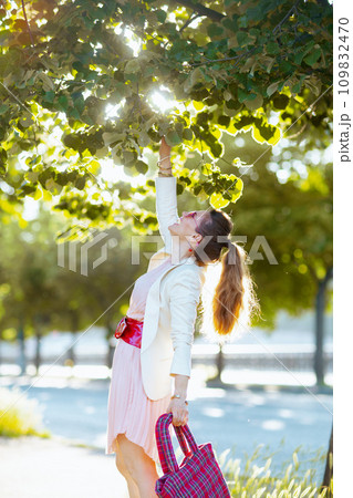 happy elegant woman in pink dress and white jacket in city 109832470