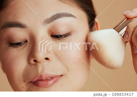 young woman with makeup brush against beige background young woman with makeup brush against beige background 109833417
