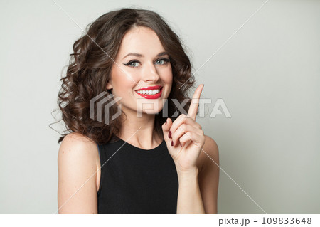 Cheerful model woman with healthy wavy hairstyle pointing finger up, studio fashion beauty portrait. 109833648