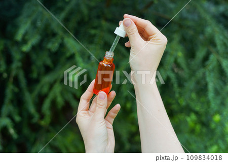 Female hands holding red glass bottle with spa cosmetic oil. salon therapy, natural eco body care products, green nature background Female hands holding red glass bottle with spa cosmetic oil. salon therapy, natural eco body care products, green nature background 109834018