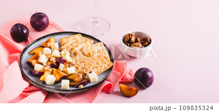 Dinner for girls, cheese, biscuits, plums on a plate and a glass of wine on the table web banner 109835324