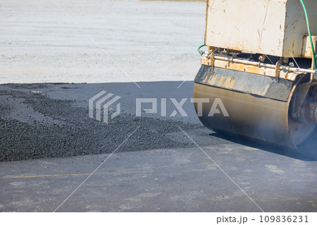 Using an asphalt vibratory roller worker lays asphalt on new road Using an asphalt vibratory roller worker lays asphalt on new road 109836231