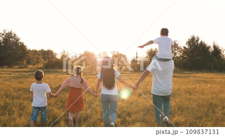 Son sits on father shoulders while family walks with across field at sunset 109837131