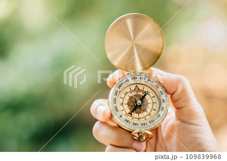 A close-up of a hand clutching a compass in the heart of a green forest. This image leaves space for text and signifies travel lifestyle and the strategic management of a thriving business. 109839968