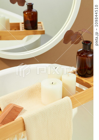 A towel covers a wooden tray, a comb, scented candles and a vase of autumn leaves. Space inside the bathroom for advertising and displaying products. A towel covers a wooden tray, a comb, scented candles and a vase of autumn leaves. Space inside the bathroom for advertising and displaying products. 109844510