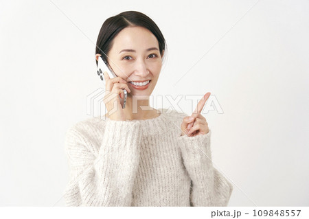 スマホで通話をしながら右側を指差す中年女性 白背景 スマホで通話をしながら右側を指差す中年女性 白背景 109848557