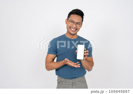 A positive, smiling Asian man is showing a smartphone to the camera, isolated white background. 109849897