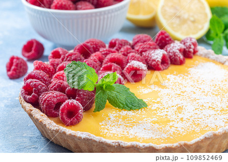 Homemade lemon tart, garnished with fresh raspberry, icing sugar, mint, horizontal closeup 109852469
