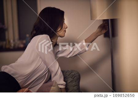ジャケットを脱いでスタンドの電気をつけるビジネスウーマンのナイトルーティーン　 109852650