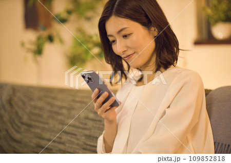 ジャケットを脱いでソファでスマホを見るビジネスウーマン のナイトルーティーン ジャケットを脱いでソファでスマホを見るビジネスウーマン のナイトルーティーン 109852818