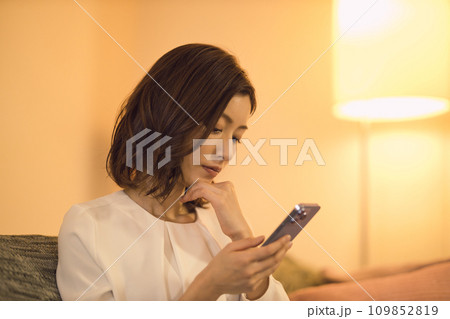 ジャケットを脱いでソファでスマホを見るビジネスウーマン のナイトルーティーン ジャケットを脱いでソファでスマホを見るビジネスウーマン のナイトルーティーン 109852819