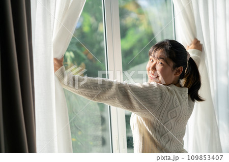 Happy woman opening window curtains in the morning at home. Happy woman opening window curtains in the morning at home. 109853407