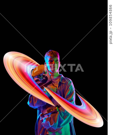 Teen boy standing with skateboard against black background in neon lights with colorful abstract element. Creative design. 109854866