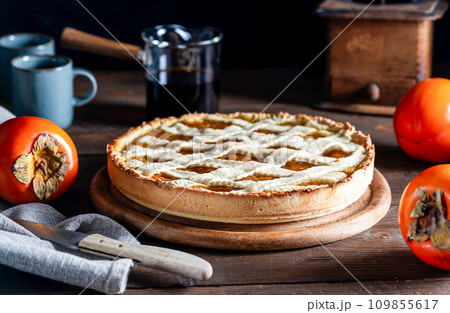 Italian homemade persimmon tart or crostata with persimmon fruits, coffee on the wooden table, chiaroscuro style 109855617