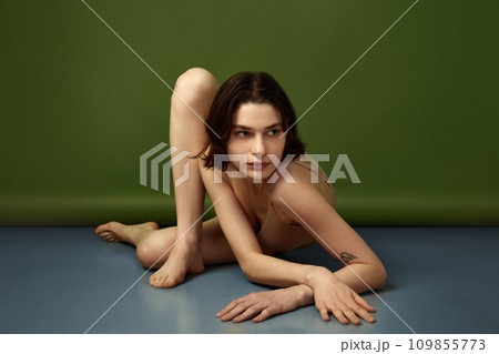 Combination of young woman's confidence who posing on floor and subtle tones of beige lingerie against olive studio background. 109855773