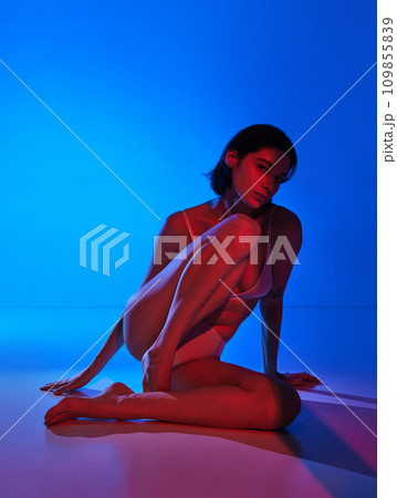 Essence of modern beauty. Young woman posing in underwear against studio background in energetic glow of mixed neon light. 109855839