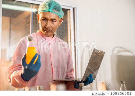 Quality officer meticulously inspects manufacturing line for top standards. Engineer diligently checks maintains machinery ensuring high-quality output in beverage bottling factory. 109856501