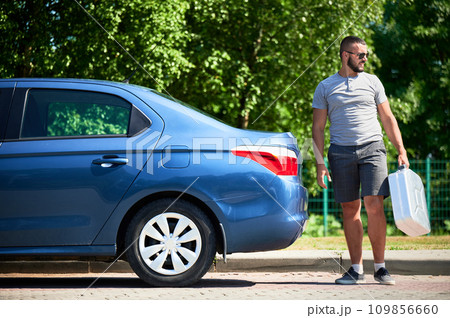 Young man looking for help with his stalled car. Male adult looking for the nearest petrol station. Man in casual clothes and sunglasses holding empty cistern and looking away. 109856660