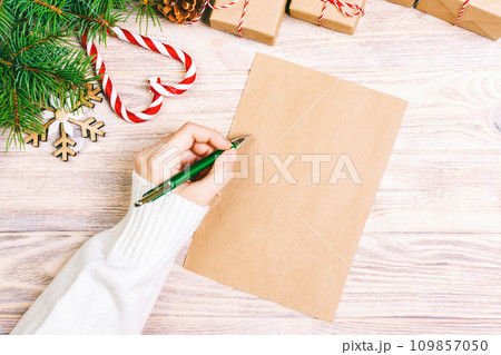 girl hand writing Christmas letter on craft paper with decorations on wooden background. Toned girl hand writing Christmas letter on craft paper with decorations on wooden background. Toned 109857050