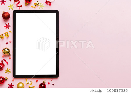 Christmas online shopping from home tablet pc with blank white display top view. Tablet with copy space on colored background with Christmas decorations balls,. Winter holidays sales background Christmas online shopping from home tablet pc with blank white display top view. Tablet with copy space on colored background with Christmas decorations balls,. Winter holidays sales background 109857386