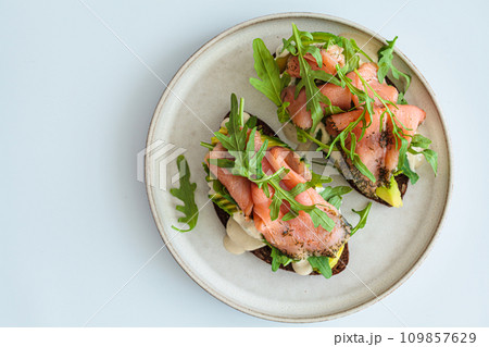 Rye toast with smoked salmon, avocado, hollandaise sauce and arugula. Rye toast with smoked salmon, avocado, hollandaise sauce and arugula. 109857629