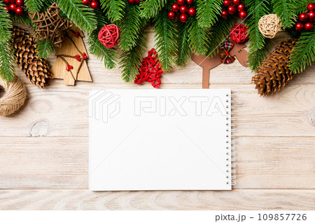 Top view of notebook, Christmas toys, decorations and fir tree branches on wooden background. New Year holiday concept 109857726