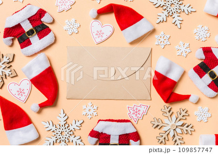 Top view of craft envelope with Christmas decorations and Santa hats on orange background. Happy holiday concept Top view of craft envelope with Christmas decorations and Santa hats on orange background. Happy holiday concept 109857747