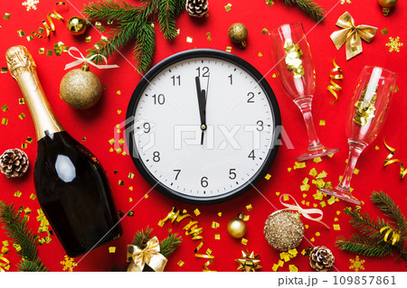 New year celebration concept with a bottle of champagne and two glasses toasting. Christmas gift box, alarm clock and fir tree branch on colored table. Top view Copy space New year celebration concept with a bottle of champagne and two glasses toasting. Christmas gift box, alarm clock and fir tree branch on colored table. Top view Copy space 109857861