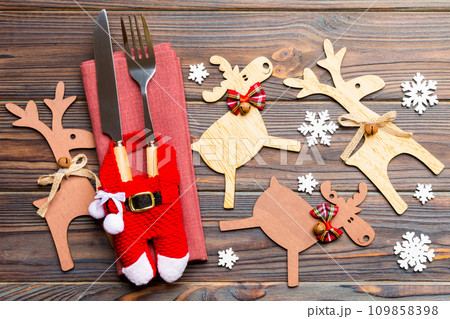 Top view of new year utensils on napkin with holiday decorations and reindeer on wooden background. Close up of christmas dinner concept 109858398