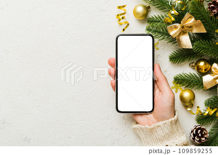 christmas mockup with space for text. christmas advertising, app template. hand holding phone with empty screen on table background. Happy New Year and Xmas Flat lay 109859255