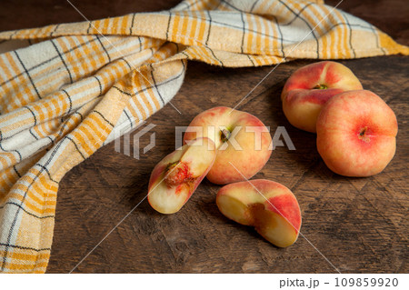 Half and three whole saturn peaches or flat peaches on wooden background with yellow kitchen towel.. Half and three whole saturn peaches or flat peaches on wooden background with yellow kitchen towel.. 109859920