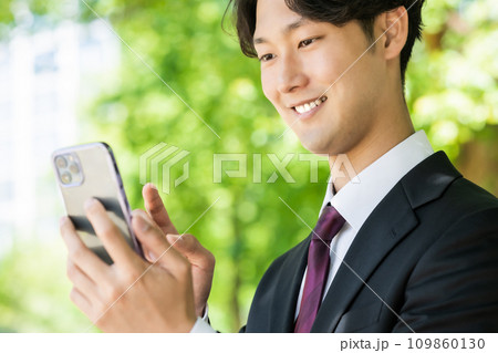 スマホを片手に外回りをする若いビジネスマン スマホを片手に外回りをする若いビジネスマン 109860130