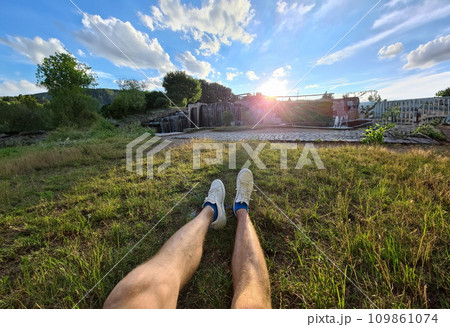 Male feet in white sneakers lying on green grass against background of waterfall closeup 109861074