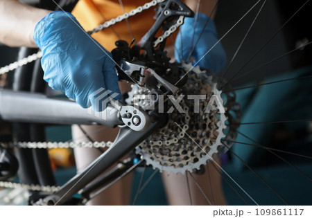 Technician in protective gloves repairing rear wheel of bicycle closeup Technician in protective gloves repairing rear wheel of bicycle closeup 109861117