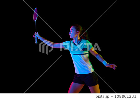 Strength and power. Dynamic movements of professional badminton player practicing with intensity against black background in neon light. 109861233