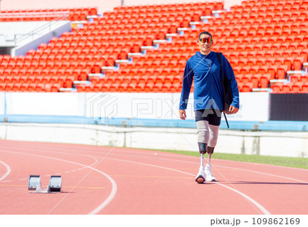 Sport man athlete prosthesis legs with sun glasses carry the bag and walk on the track of the stadium with day light. 109862169