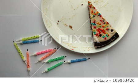 conceptual background on the theme of loneliness and the end of the holiday, top view of the last piece of birthday cake on a white dirty plate with traces of candles conceptual background on the theme of loneliness and the end of the holiday, top view of the last piece of birthday cake on a white dirty plate with traces of candles 109863420