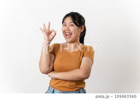 The cheerful young Asian woman smiling and showing the OK hand sign standing on white background. The cheerful young Asian woman smiling and showing the OK hand sign standing on white background. 109863560