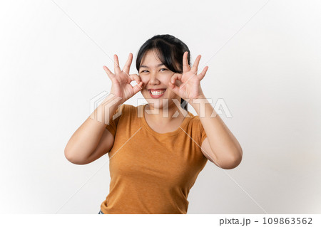 The cheerful young Asian woman smiling and showing the OK hand sign standing on white background. 109863562