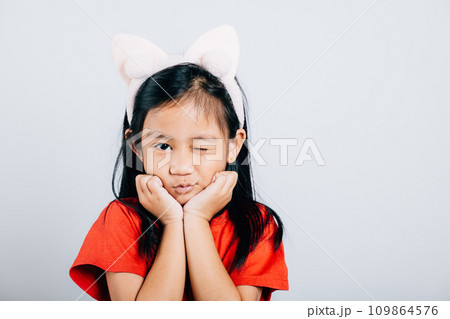An adorable Asian girl child laughs with delight showcasing a broad smile and cheerful eyes. Isolated portrait of a happy open-mouthed kid in a red t-shirt on a white background. 109864576