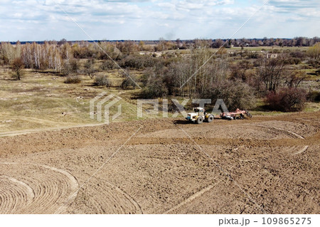 Agricultural machinery in a field near a small grove, aerial view. Agricultural land. Agricultural machinery in a field near a small grove, aerial view. Agricultural land. 109865275