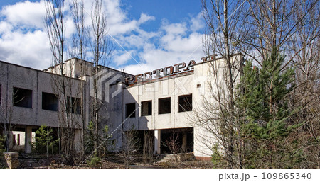 A dilapidated building with the word on top, surrounded by bare trees and overgrown vegetation. An abandoned restaurant in Pripyat. Ruins of a building in a city contaminated with radiation. 109865340