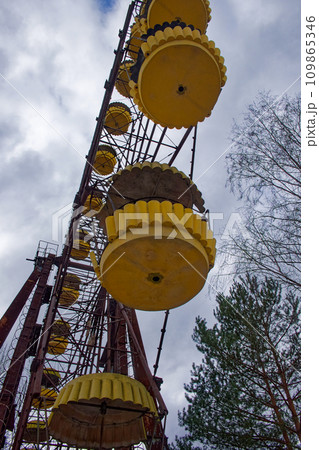 A rusted, abandoned yellow ferris wheel with empty seats surrounded by overgrown vegetation. A rusted, abandoned yellow ferris wheel with empty seats surrounded by overgrown vegetation. 109865346
