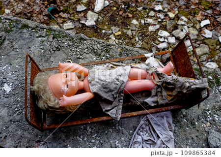 A discarded doll lies in a rusty bed amidst debris. 109865384