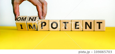 Hand is turning cubes and changes the word 'impotent' to 'omnipotent' or vice versa. Beautiful yellow table, white background. Medical concept. Copy space. 109865703