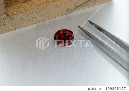 macro mineral faceted stone Garnet with tweezers on a gray background 109866197