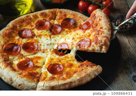 A slice of hot Italian pizza with stretching cheese. Pizza pepperoni on a dark wooden background A slice of hot Italian pizza with stretching cheese. Pizza pepperoni on a dark wooden background 109866431