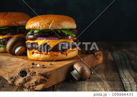 Two delicious homemade burgers of beef, cheese and mushrooms on an wooden table. With copy space Two delicious homemade burgers of beef, cheese and mushrooms on an wooden table. With copy space 109866435