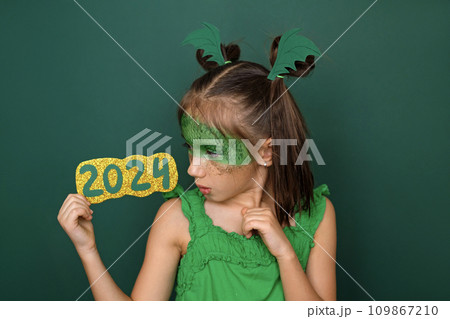 A child dressed up as a dragon looks with surprise at the numbers 2024. Waiting for the new Year A child dressed up as a dragon looks with surprise at the numbers 2024. Waiting for the new Year 109867210